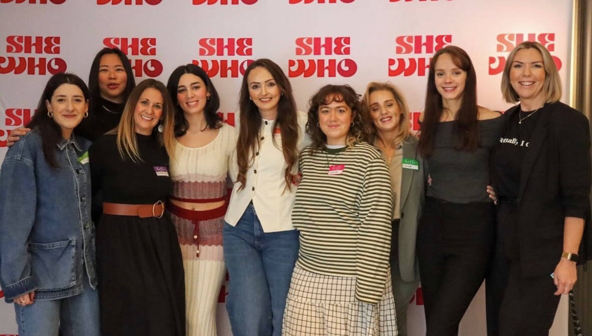 The She Who community together at an event, in front of the #SHEWHO backdrop